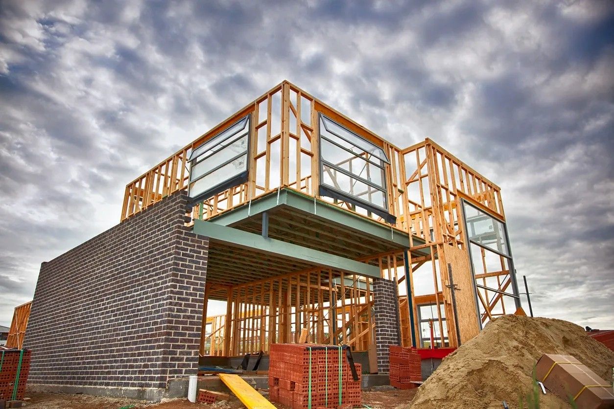 A two-storey commercial building under construction — wood framing over a brick base against a dramatic cloudy sky
